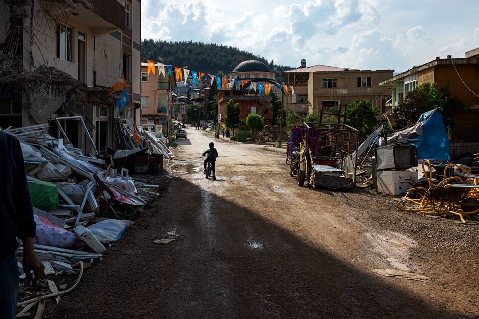 Lapsi pyöräilemässä romahtaneiden talojen ohi İslahiyen kaupungissa. Kadun yllä roikkuvat AK-puolueen liput.