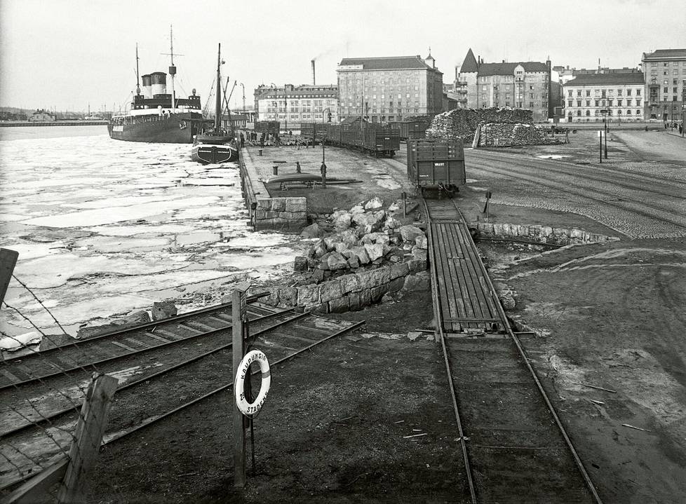 Hietalahtenranta 15 with its corner towers (top right), siding of the harbor railway, stacks of logs and breaker Jääkarhu at Hietalahten pier. 