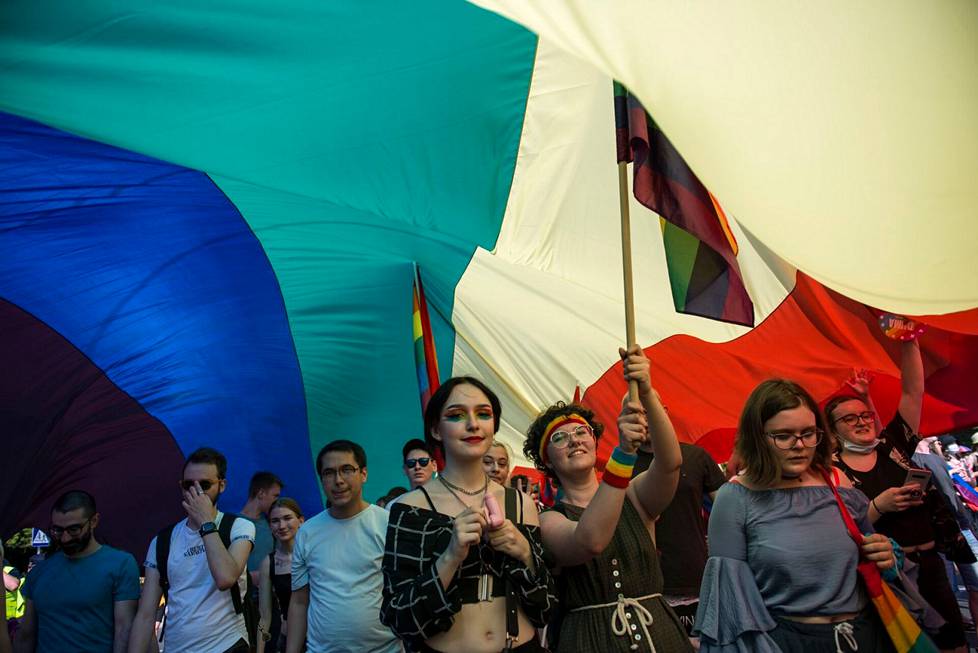 Mielenosoittajat marssivat valtavan sateen­kaari­lipun alla Puolan Varsovassa 19. kesäkuuta.