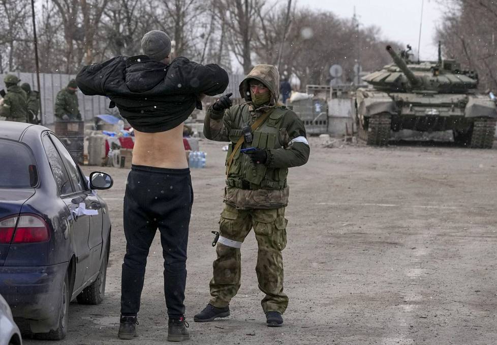Itä-Ukrainan separatistijoukkojen sotilas tarkasti Mariupolista pakenevaa siviilimiestä kaupungin ulkopuolella sijaitsevalla tarkastuspisteellä sunnuntaina.